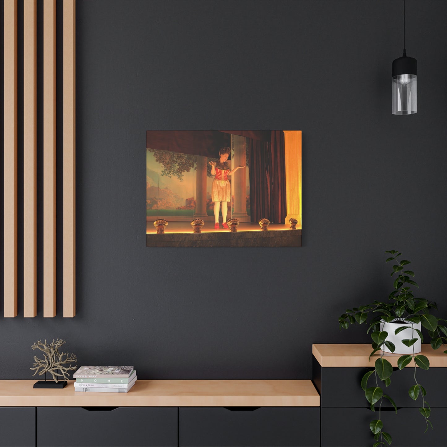 A framed art print depicting a classical scene with a figure in a red dress standing in a doorway, displayed on a dark gray wall in a modern room setting with a wooden console, plants, and a hanging light.
