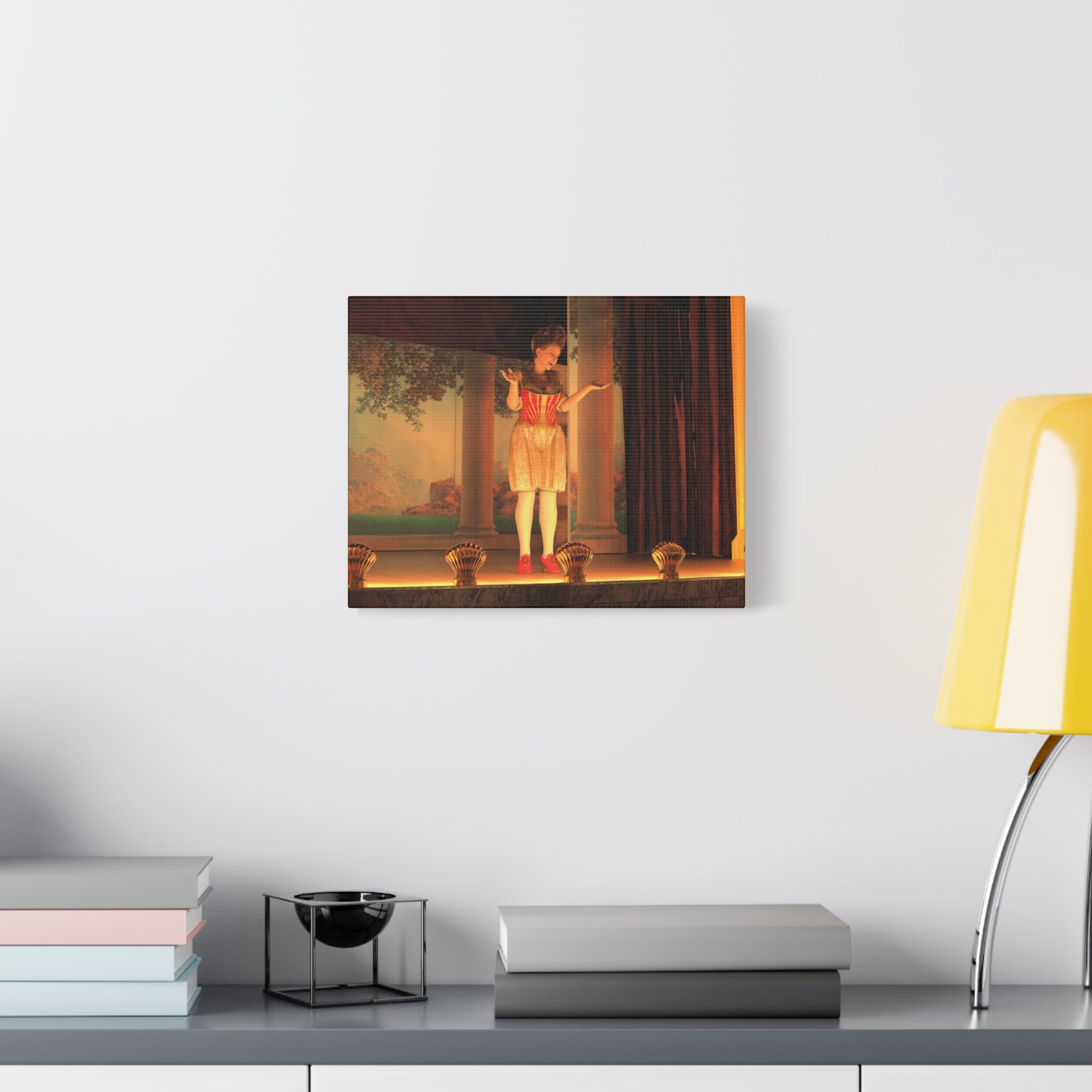 A framed wall art print depicting a ballerina on a stage, displayed on a light gray wall above a shelf with books and a yellow lamp.