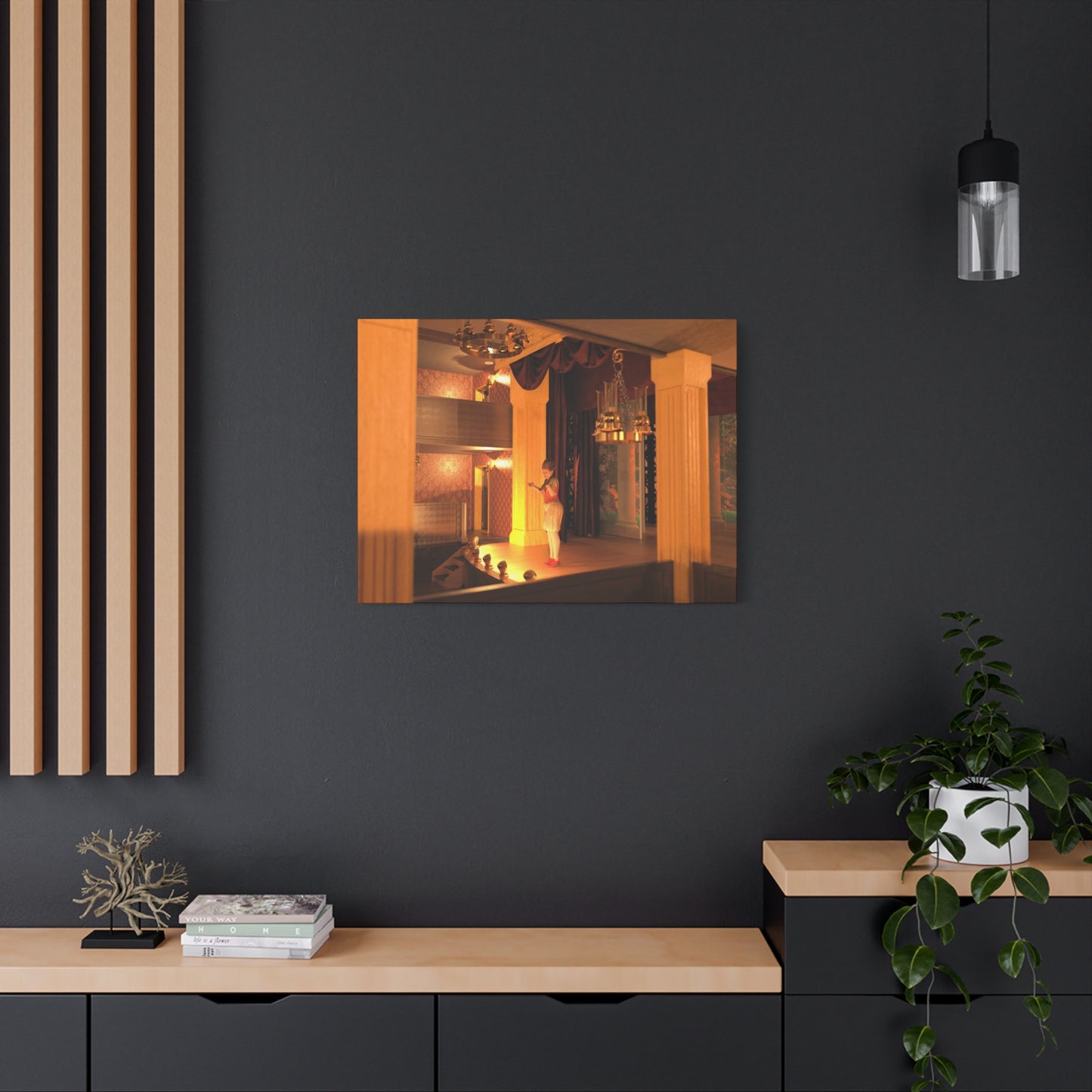 A rectangular wall art print showing a warmly lit interior scene with orange and yellow tones, displayed on a dark charcoal wall above a light wood console. The room includes decorative wall slats, a hanging lamp, books, and a potted plant.